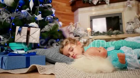 孩子睡在圣诞树附近小可爱的女孩在睡觉时抱着一个娃娃在客厅里睡得很香视频的预览图