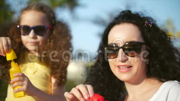 一家人开心地笑着妈妈和女儿在玩耍在夏天的户外吹肥皂泡库存录像视频的预览图