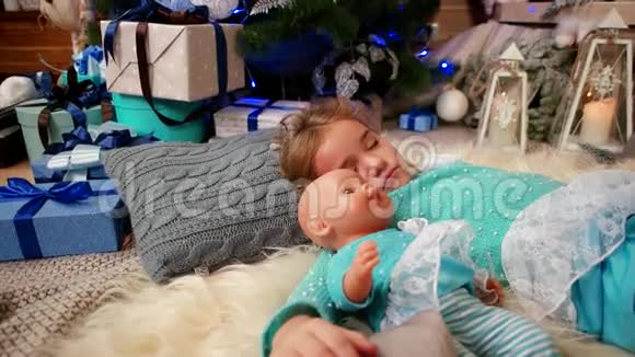 小可爱的女孩睡在壁炉旁火炉旁抱着一个娃娃孩子睡在圣诞树旁视频的预览图