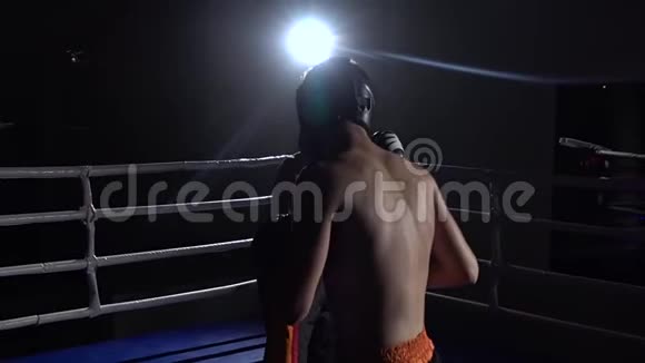 两个戴着头盔和拳击手套的人在黑暗中在擂台上战斗慢动作视频的预览图