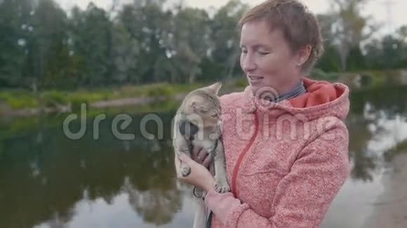 快乐的年轻女子在森林河附近展示英国的肖肖尔塔比猫户外视频的预览图
