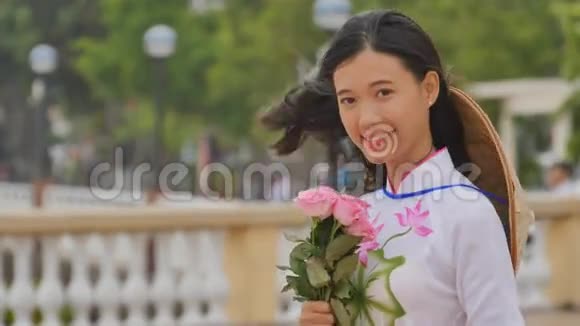 越南女孩穿着民族服装和服装为相机摆姿势和微笑手里拿着粉红色视频的预览图