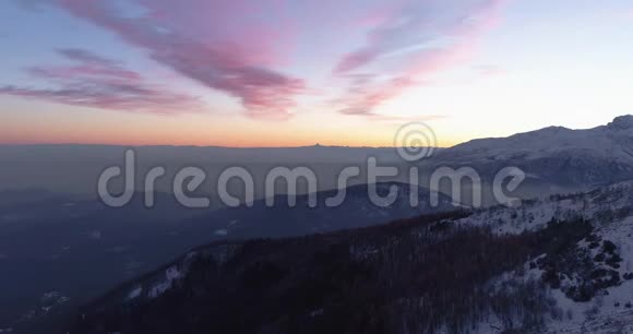 在日落或日出时在冬季雪山和森林的背面俯视黄昏或黎明视频的预览图