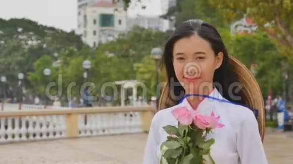 越南女孩穿着民族服装和服装为相机摆姿势和微笑手里拿着粉红色视频的预览图