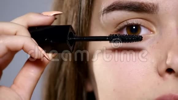 面部化妆年轻的深色女人用黑色睫毛膏为她的长睫毛画上一张特写镜头4K视频的预览图