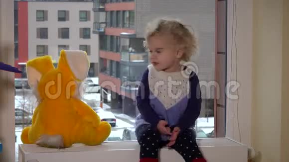 小女孩和兔子朋友坐在窗边看着雪花视频的预览图