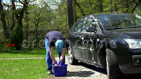 年轻人用肥皂海绵洗他的黑色汽车视频的预览图