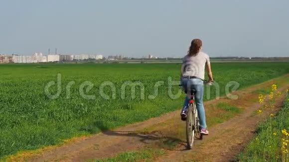 大自然中骑自行车的女孩一个女人在城外骑自行车油菜田乡村公路视频的预览图