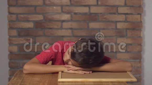 坐在办公桌前的孩子拿着一张挂图在背景红砖墙上醒来视频的预览图
