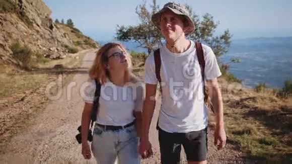 年轻的时髦情侣在日落的山路上徒步旅行视频的预览图