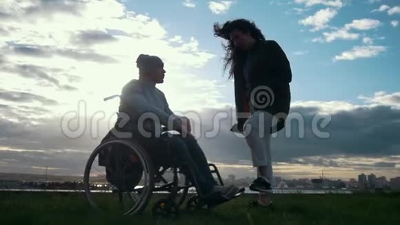 照顾残疾人坐轮椅的男人和女人在阴天日落时交谈视频的预览图