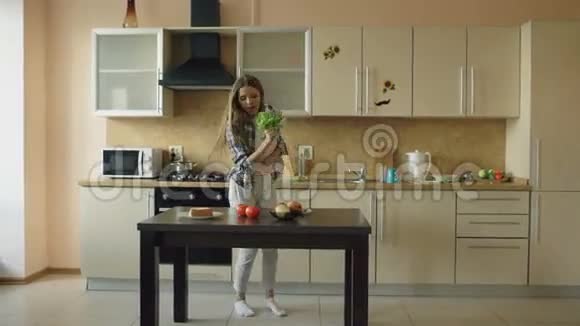 快乐的年轻有趣的女人在做早餐时用莴苣麦克风跳舞唱歌视频的预览图