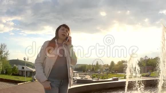 一个女人在喷泉前通过电话交流视频的预览图