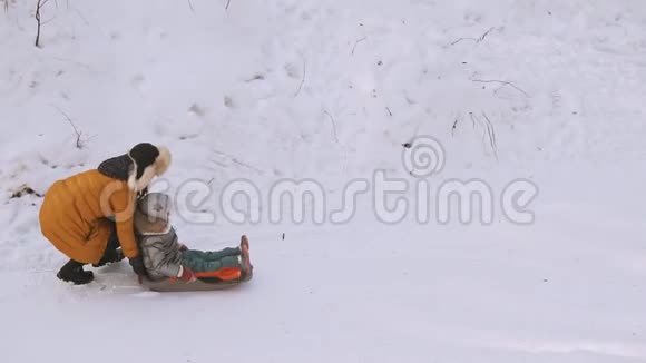 母亲和女儿在冬季公园的雪橇上玩得很开心寒冷的雪天视频的预览图