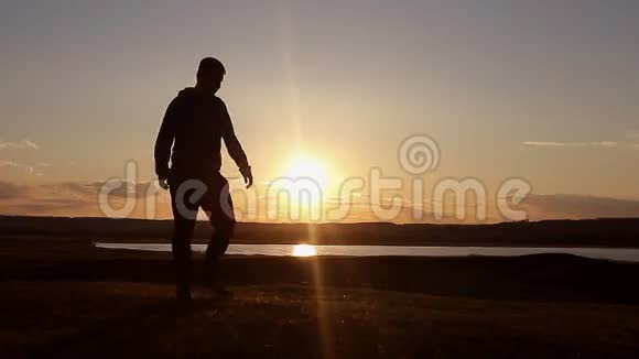 人走在夏日草甸夕阳西下山顶上年轻人的剪影视频的预览图