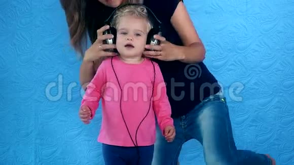 女人把大耳机放在女孩的头上孩子喜欢音乐视频的预览图
