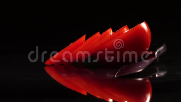 在黑色背景的黑色桌子上用一把旋转的刀切割成熟的番茄视频的预览图