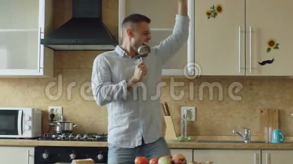 在家厨房做饭时有魅力的年轻滑稽男子用勺子跳舞唱歌视频的预览图