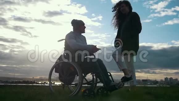坐轮椅的残疾人和女人在阴云密布的夕阳下交谈视频的预览图