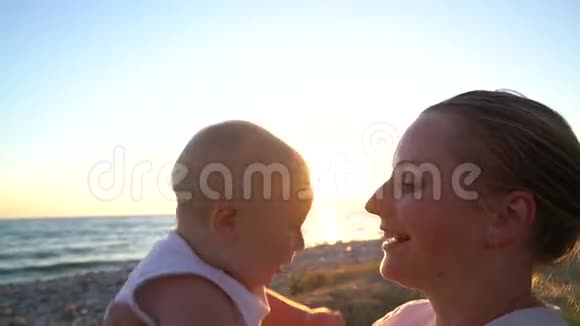 妈妈在日落时分和一个孩子坐在沙滩上视频的预览图