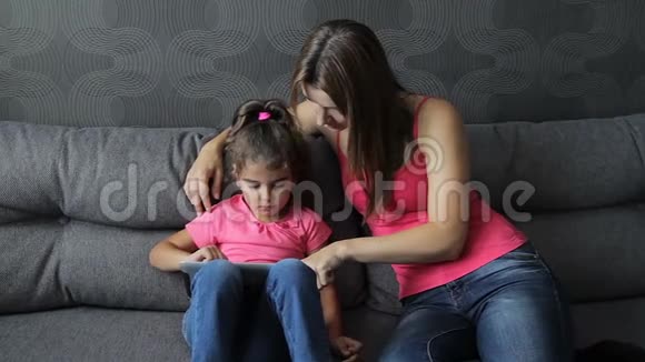 有孩子的女人用平板电脑坐在沙发上母亲带着孩子坐在沙发上用平板电脑视频的预览图