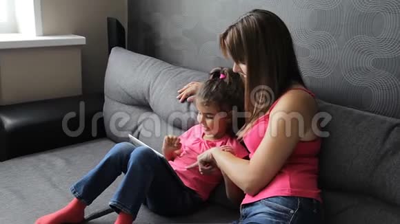 有孩子的女人用平板电脑坐在沙发上母亲带着孩子坐在沙发上用平板电脑视频的预览图