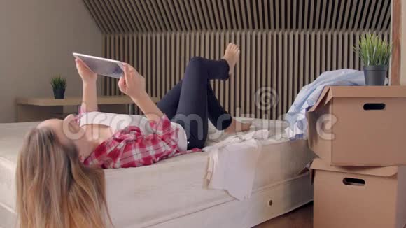 女人躺在床上用数码平板电脑而不是在新家拆箱视频的预览图