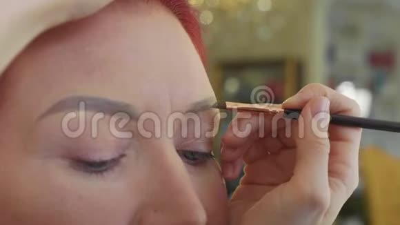 化妆师给美容店的年轻红发女人做漂亮的眉毛视频的预览图