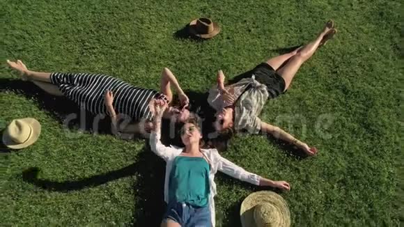 三个迷人的女孩躺在绿草上在阳光明媚的草地上玩得开心山的背景视频的预览图