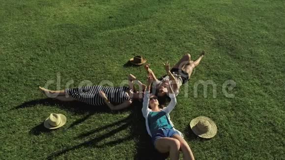 三个迷人的女孩躺在绿草上在阳光明媚的草地上玩得开心山的背景视频的预览图