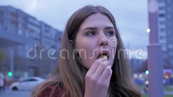 一个年轻女孩在城镇广场吃快餐年轻女子站在城市街道上吃薯条青年视频的预览图