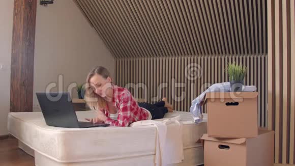 年轻的金发女人躺在床上早上在笔记本电脑上工作手持射击视频的预览图