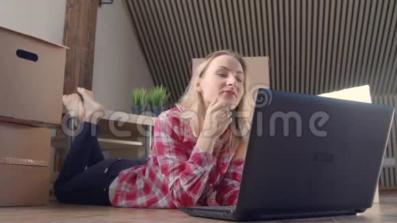 美丽的女人正在使用笔记本电脑兴奋地微笑着找到新的东西而坐在移动的盒子附近的地板上视频的预览图