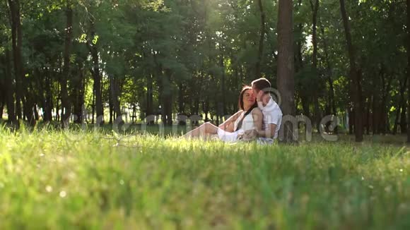 幸福的一对夫妇坐在靠近树的公园里的草地上视频的预览图