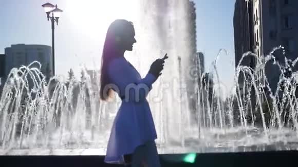 美丽苗条的女孩站在喷泉附近手里拿着电话写着一条信息电话反射光线视频的预览图