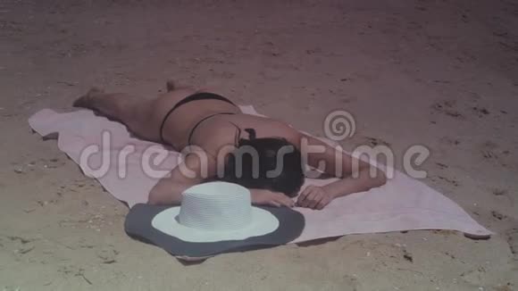 夏天阳光明媚的一天穿着黑色泳衣和帽子的浅黑女孩在海边晒太阳视频的预览图