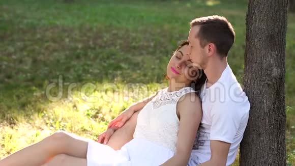 幸福的一对夫妇坐在靠近树的公园里的草地上视频的预览图