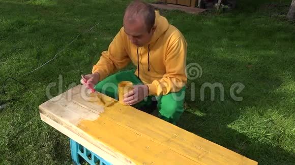 男性杂工用刷子和油漆罐在手中油漆木板表面黄色4K视频的预览图