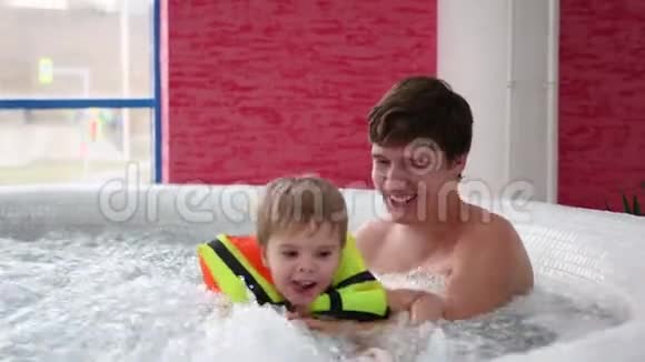 一位带着孩子的年轻父亲在水疗池里游泳在游泳池里放松和娱乐视频的预览图