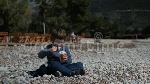 一个小男孩坐在岩石上高兴地吃奶油视频的预览图