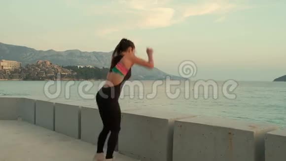 年轻苗条的女子穿着训练服跳在海堤上的石头上视频的预览图