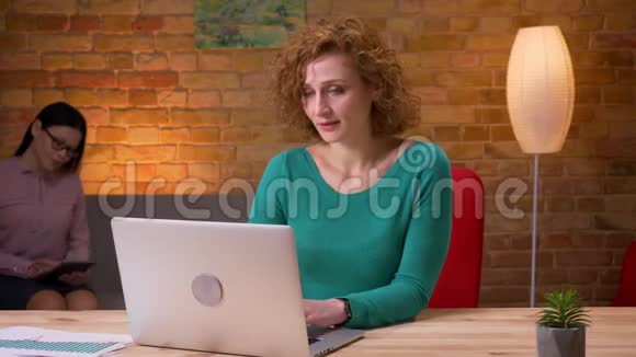 在办公室里一位成年女商人在笔记本电脑上打字看着相机微笑着在室内拍摄女性视频的预览图