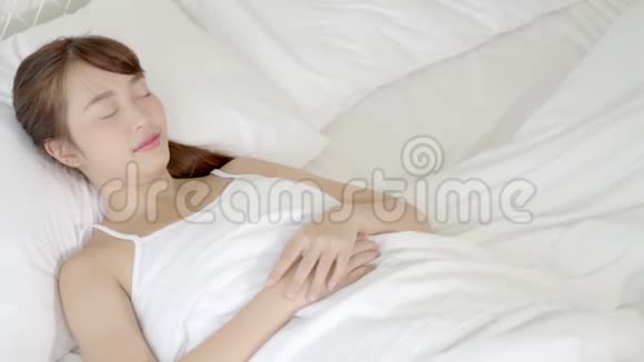 美丽的亚洲年轻女子躺在床上头靠在枕头上舒适而快乐地移动着照相机视频的预览图