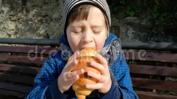 小男孩喜欢坐在户外长凳上吃大羊角面包视频的预览图