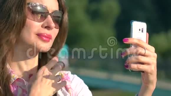 戴墨镜的漂亮黑发女孩用手机在大公园喷泉拍照4K视频视频的预览图