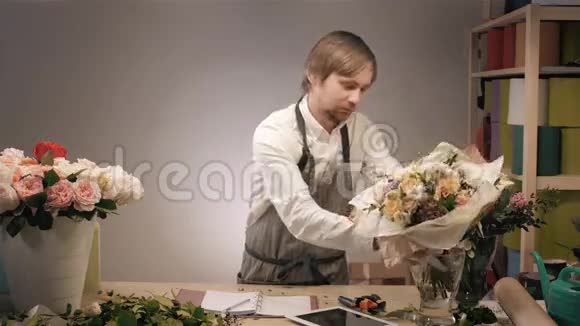 微笑的花匠站在花店里捧着一束五颜六色的花有玫瑰花豌豆紫丁香和视频的预览图