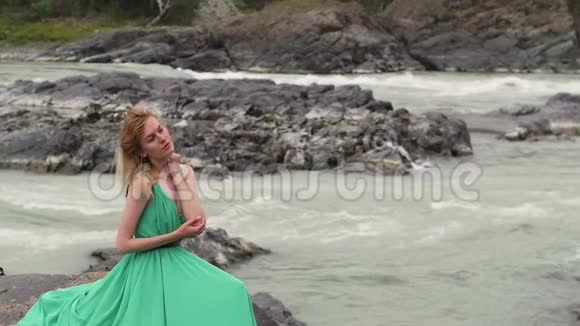 年轻的女人穿着一件长长的流动的衣服在河山的背景上穿绿色衣服的有色女人视频的预览图