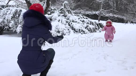 快乐的女婴在冬天的雪上向母亲走去4K视频的预览图