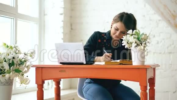 年轻漂亮的女学生坐在室内的咖啡馆里写书视频的预览图