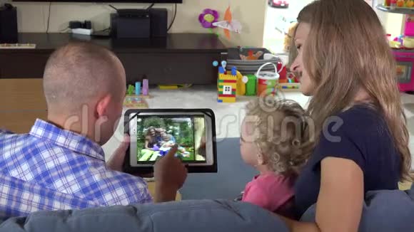 一个男人和一个蹒跚学步的女孩在家看平板电脑上的家庭照片视频的预览图
